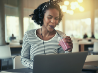 woman wearing headphones drinking strawberry milkshake and playing on her laptop